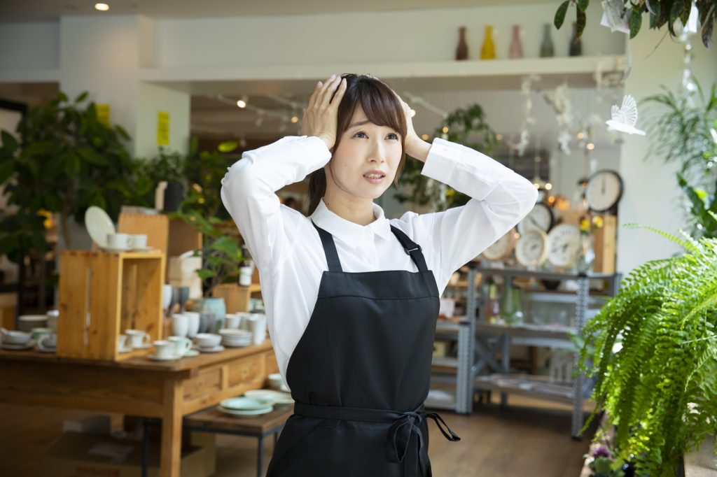 空き家活用や店舗運営での失敗事例・悩みをイメージさせる、頭を抱えて困惑するエプロン姿の女性