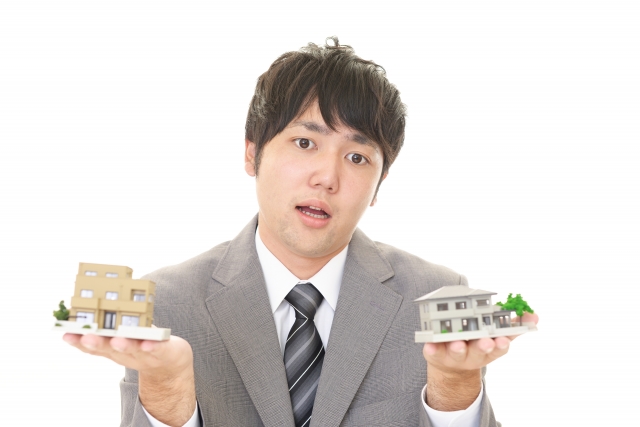 両手に家を持ち悩む男性