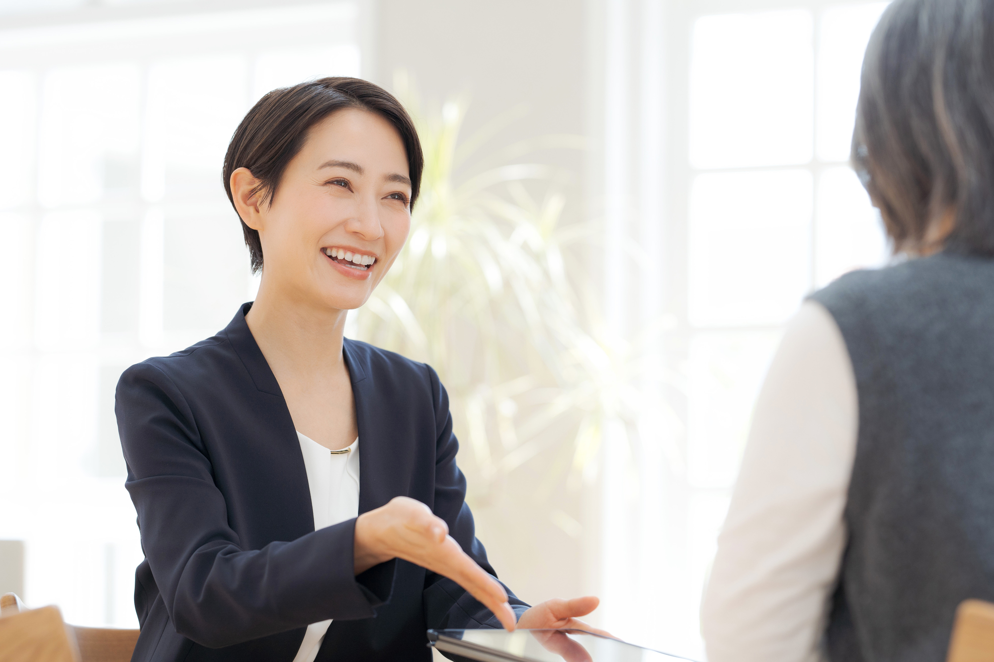 テーブル越しに笑顔で説明するスーツ姿の女性