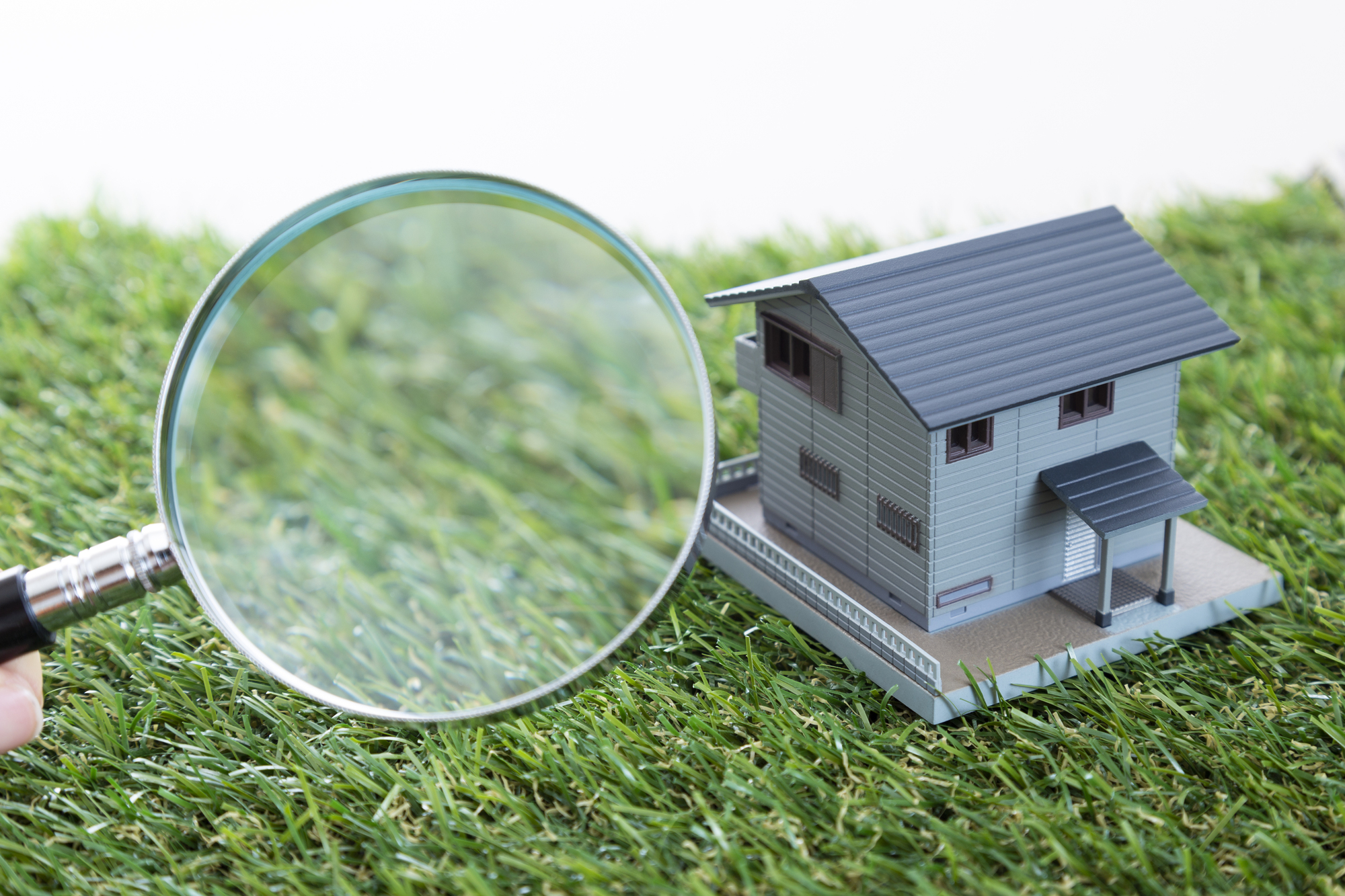 芝生の上に置かれた住宅模型と虫眼鏡