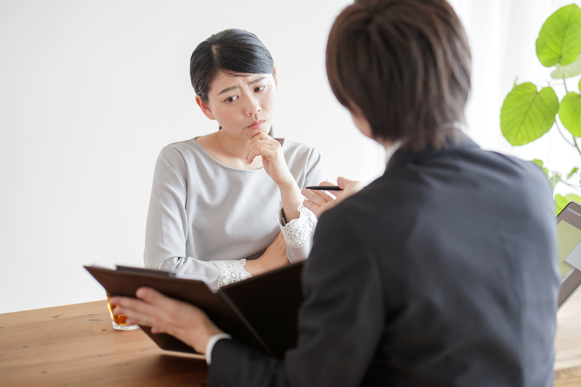 資料を持つ相談相手の説明を、顎に手を当てて聞く女性