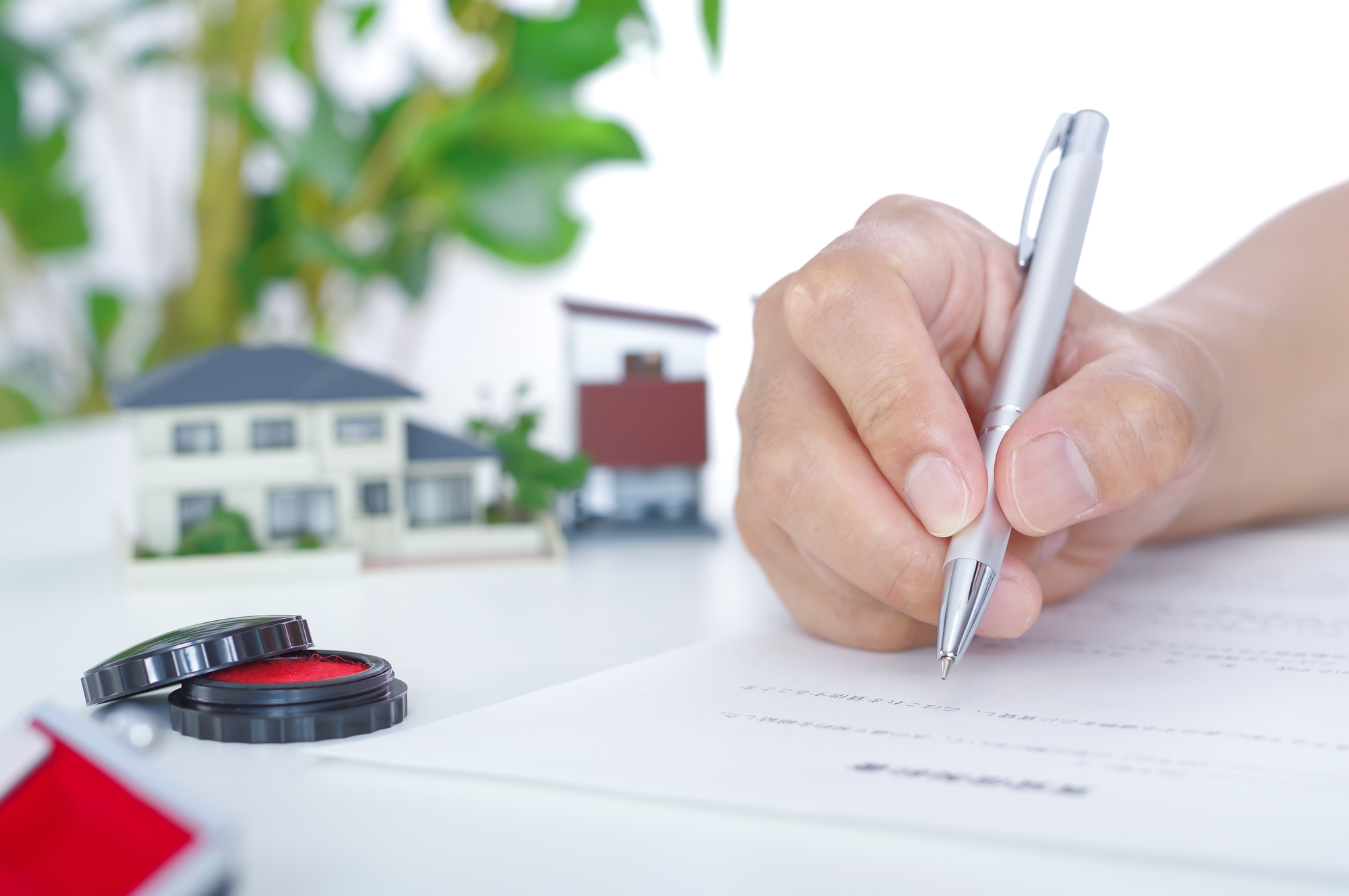 住宅模型と印鑑をそばに置き、書類に記入する手元
