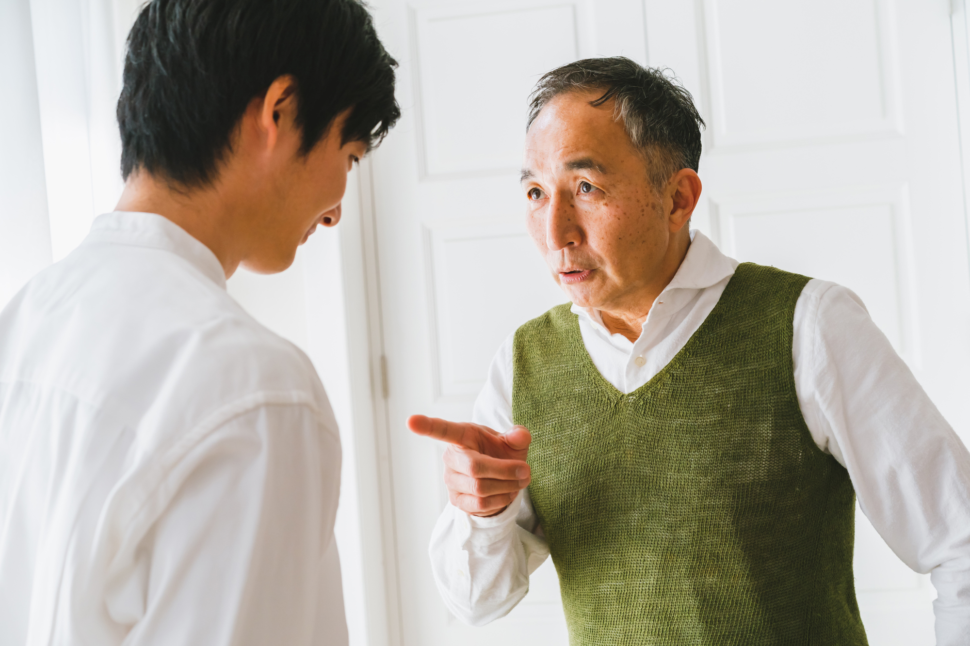 向かい合って話し、人差し指を向ける高齢の男性と若い男性
