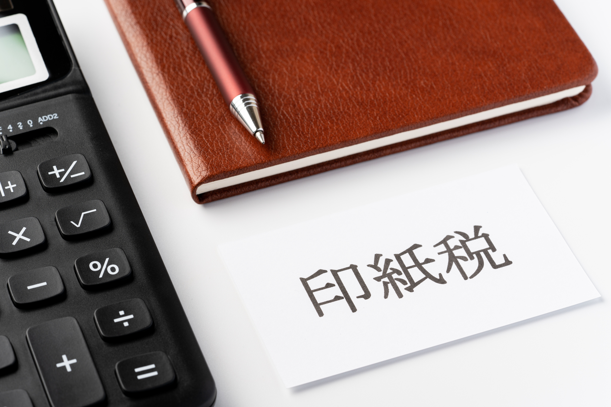 「印紙税」と書かれた紙と電卓、手帳、ペン