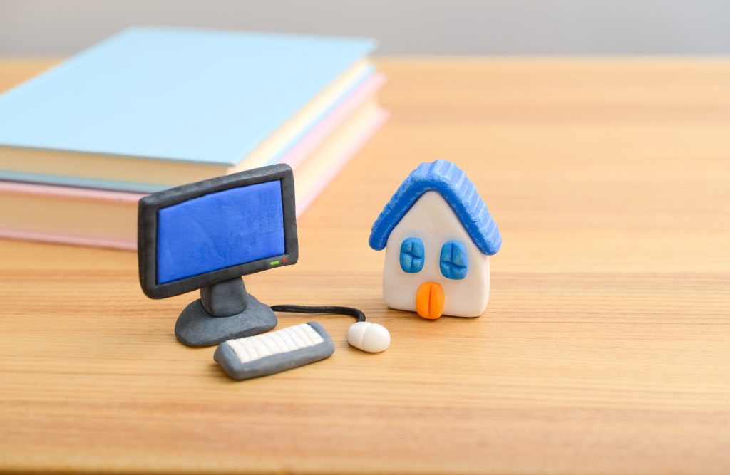 自治体サイトやマッチングサイトでの体験移住探しを表現したパソコンと家のミニチュア