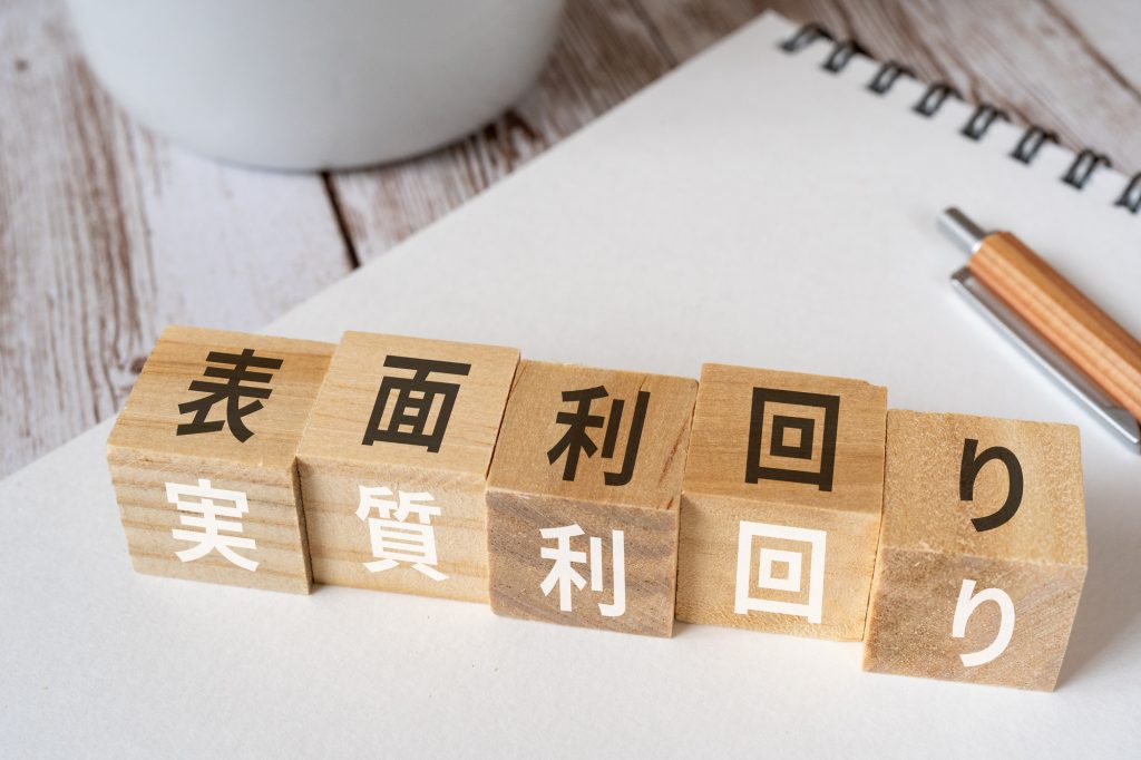 木製ブロックに書かれた表面利回りと実質利回りの文字(不動産投資の利回りの違いを比較するイメージ)