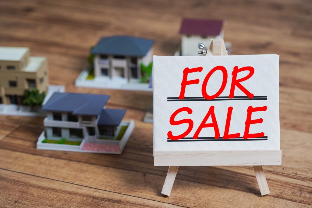 複数の住宅のミニチュア模型と「FOR SALE」と書かれたミニイーゼル（利回りが低くても検討したい物件の特徴のイメージ）
